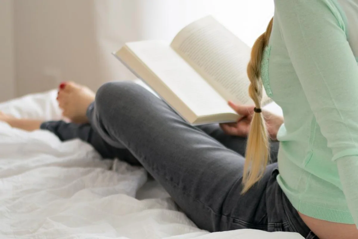 Chica con trenza leyendo un libro sentada en su cama