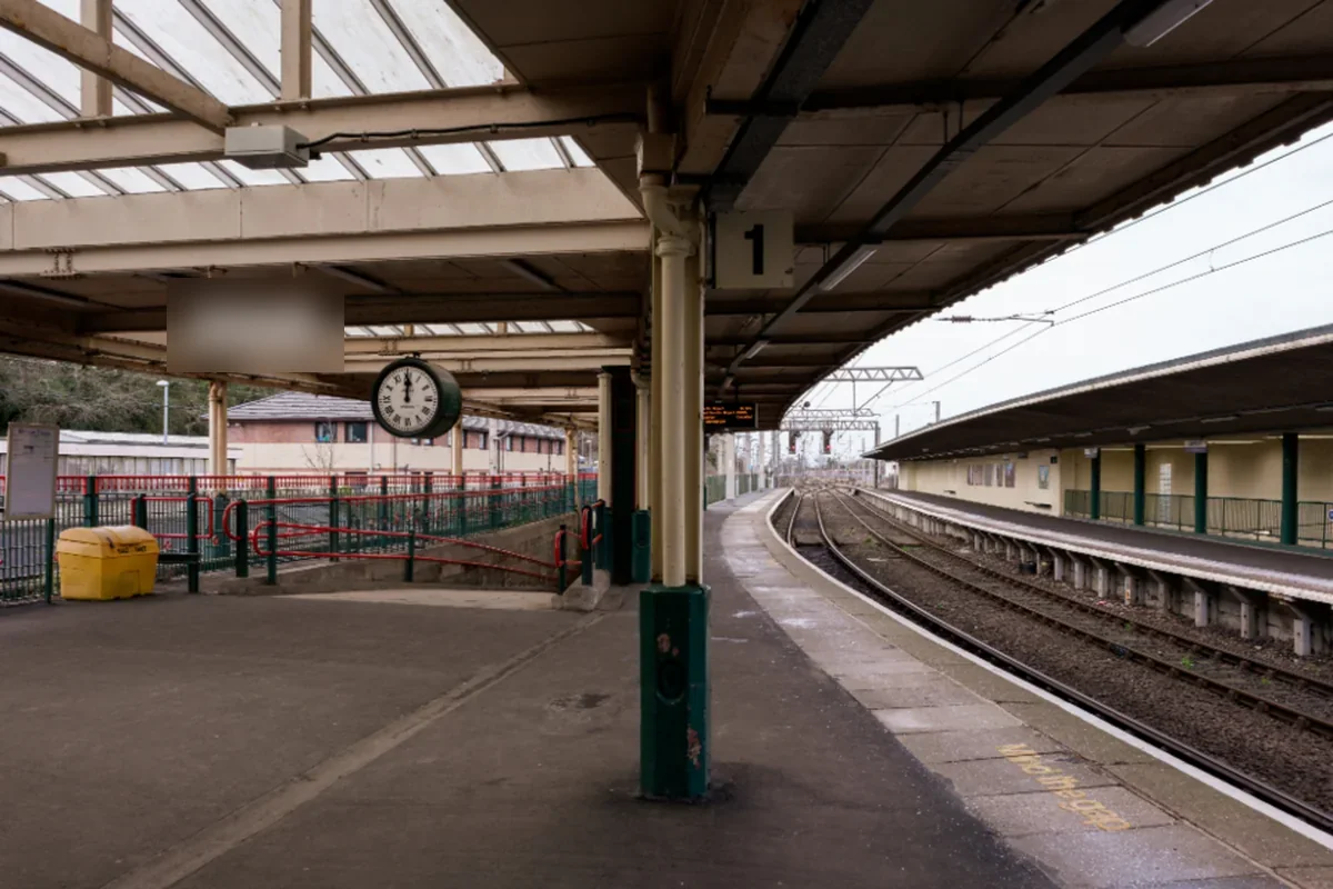 Andén vacío de una estación de tren cubierta, con un reloj colgado del techo y las vías curvándose al fondo