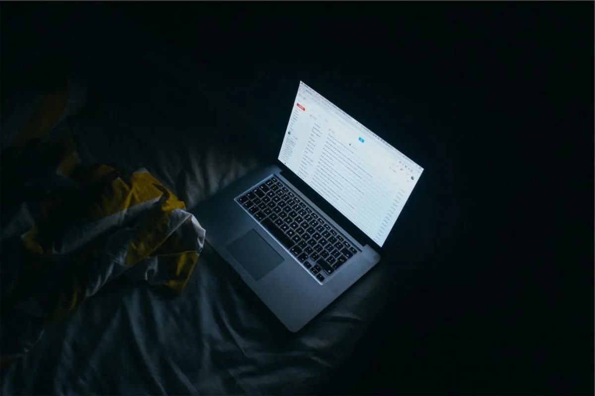 Ordenador portátil encendido sobre una cama a oscuras