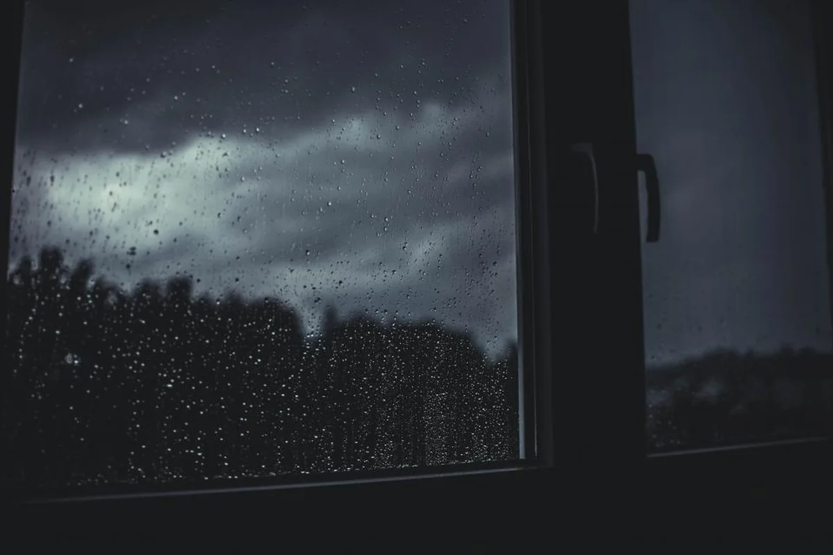 Ventana de un dormitorio a oscuras con gotas de lluvia y el cielo nocturno al fondo