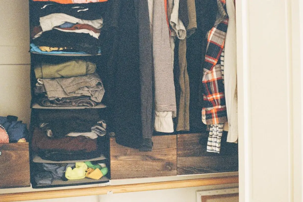 Armario abierto con ropa doblada en estantes de tela y camisas y jerséis colgados en perchas