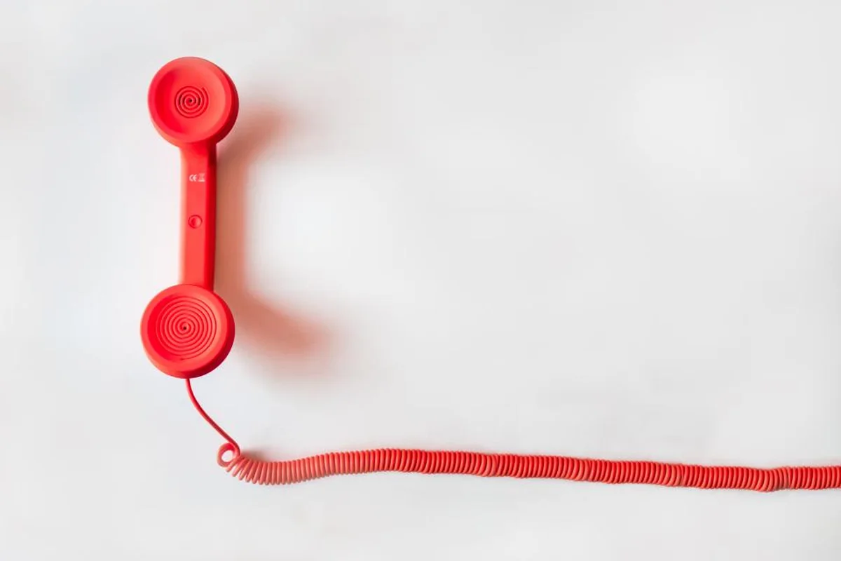 Auricular de teléfono rojo con su cable en espiral sobre un fondo blanco