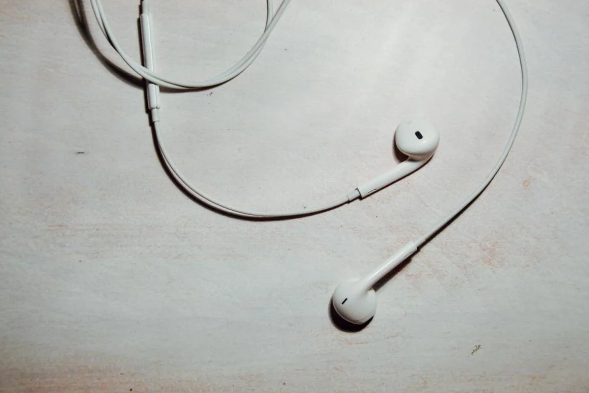 Auriculares blancos de botón con el cable enredado sobre una superficie clara
