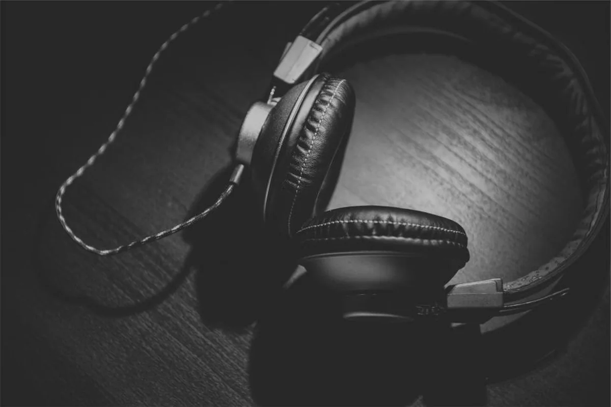 Unos auriculares negros de diadema con el cable enrollado sobre una mesa de madera en penumbra, en blanco y negro