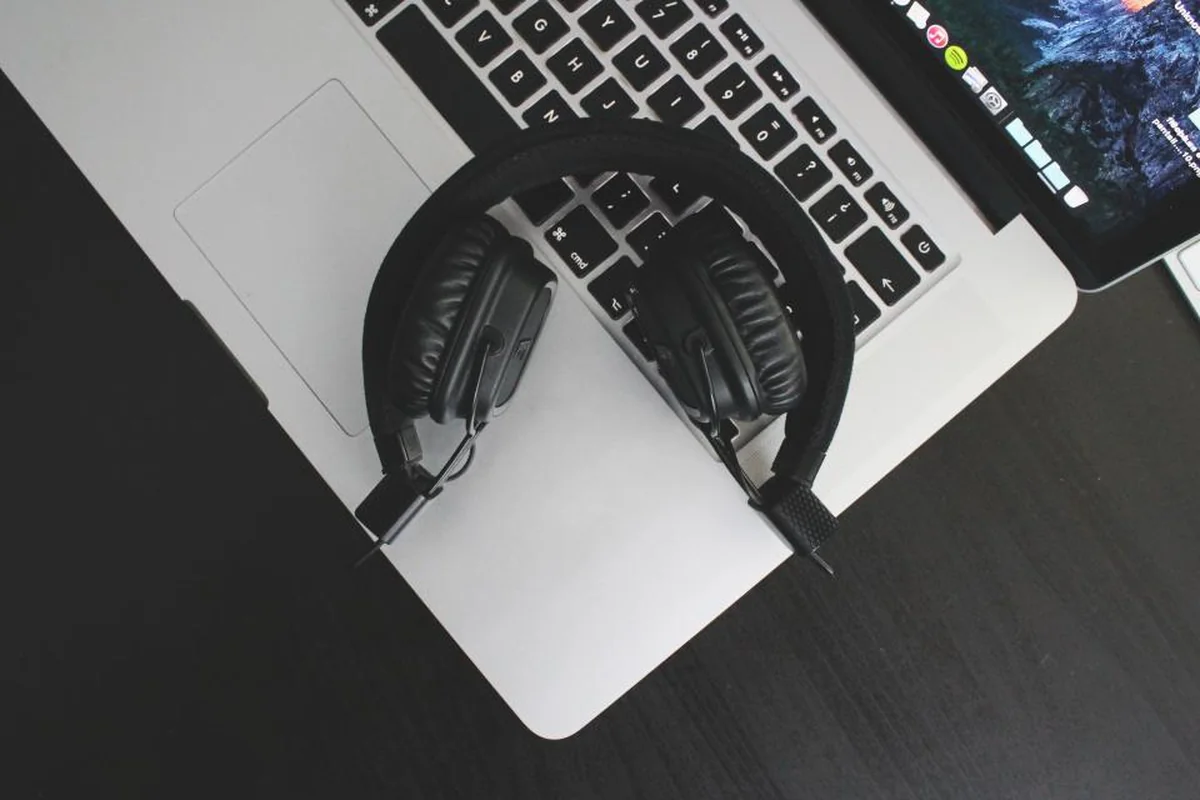 Auriculares negros apoyados sobre el teclado de un portátil abierto encima de una mesa oscura