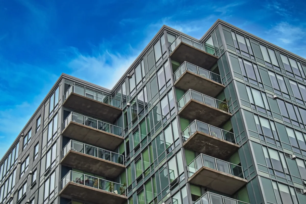 Edificio alto de fachada de cristal con varias filas de balcones, fotografiado desde abajo con el cielo azul de fondo
