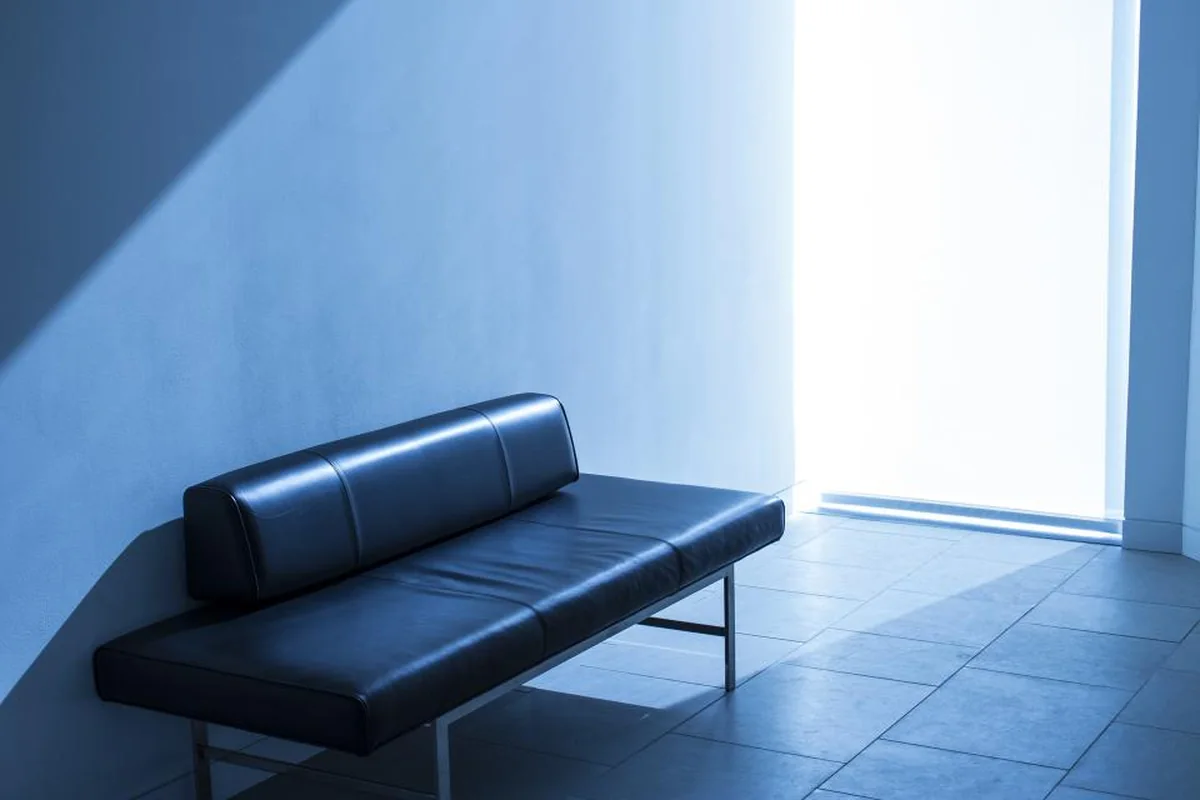 Banco de cuero oscuro vacío junto a una pared, iluminado por la luz fría y azulada de una ventana
