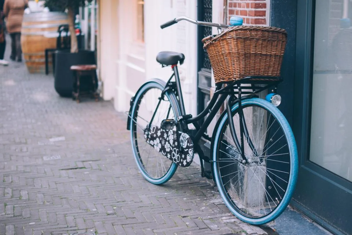 Bicicleta negra con cesta de mimbre apoyada en la fachada de una calle adoquinada
