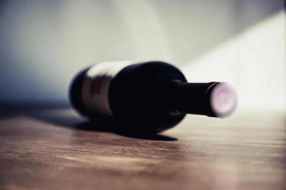 Botella de vino oscura tumbada sobre una mesa de madera, iluminada por una luz lateral suave