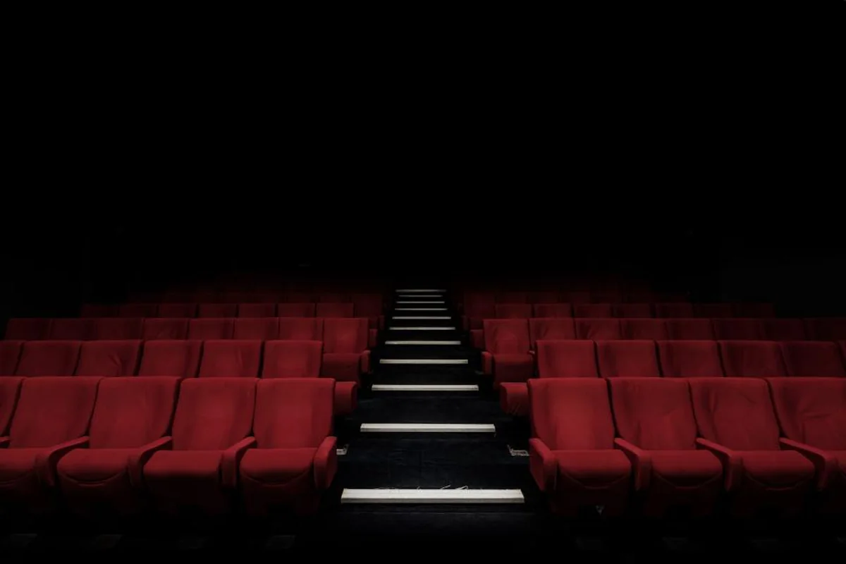 Patio de butacas rojas vacías en un teatro a oscuras con una escalera central iluminada
