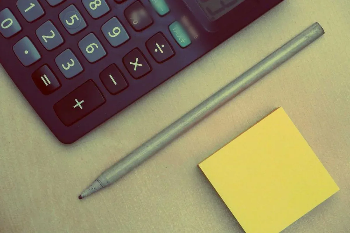 Teclado de una calculadora junto a un lápiz gris y una nota adhesiva amarilla sobre una mesa