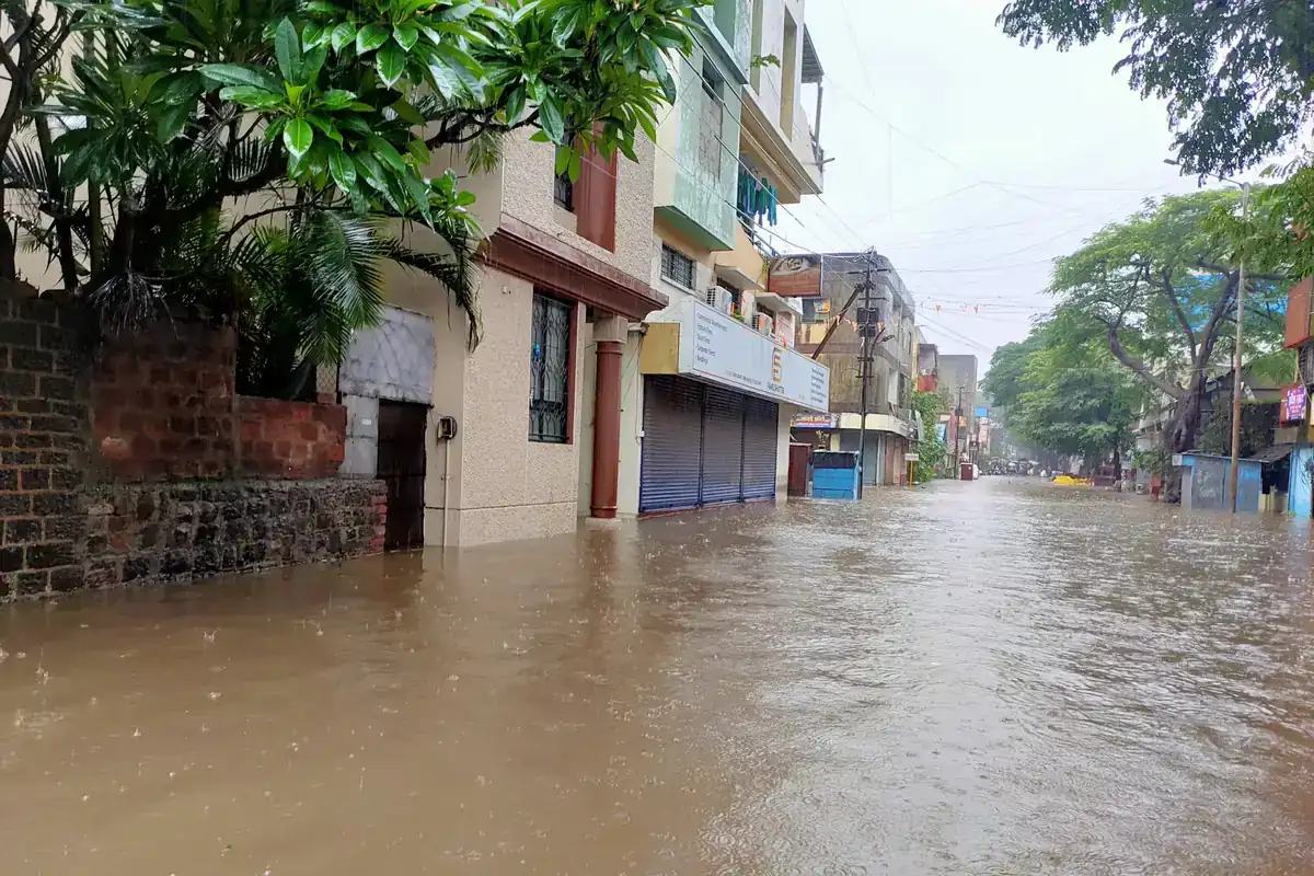 Calle anegada por agua marrón entre edificios bajos, con los comercios cerrados y árboles a los lados