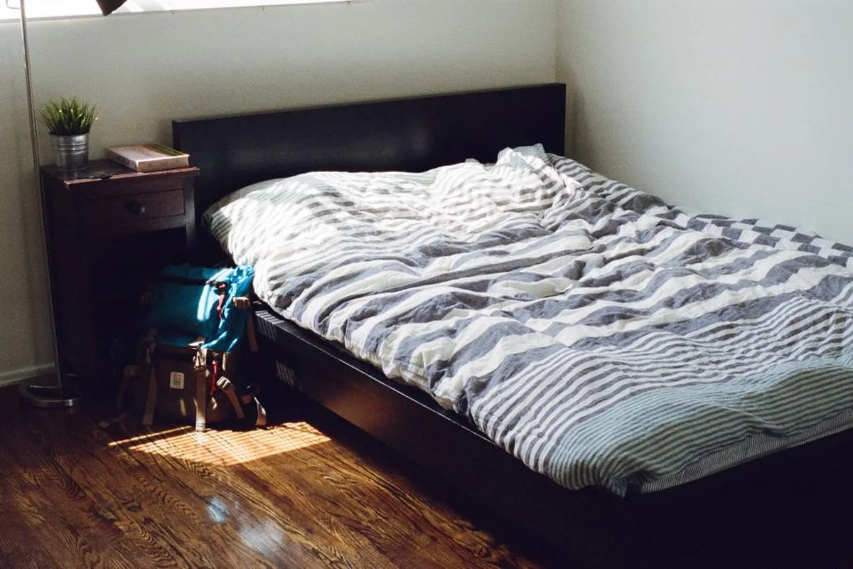Cama deshecha con funda nórdica de rayas grises y luz de mañana sobre el suelo de madera