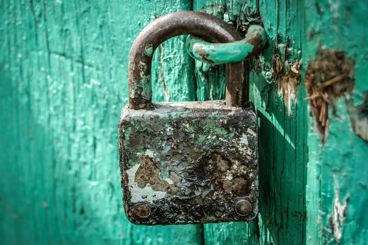 Candado viejo y oxidado cerrando una puerta de madera pintada de verde y desconchada