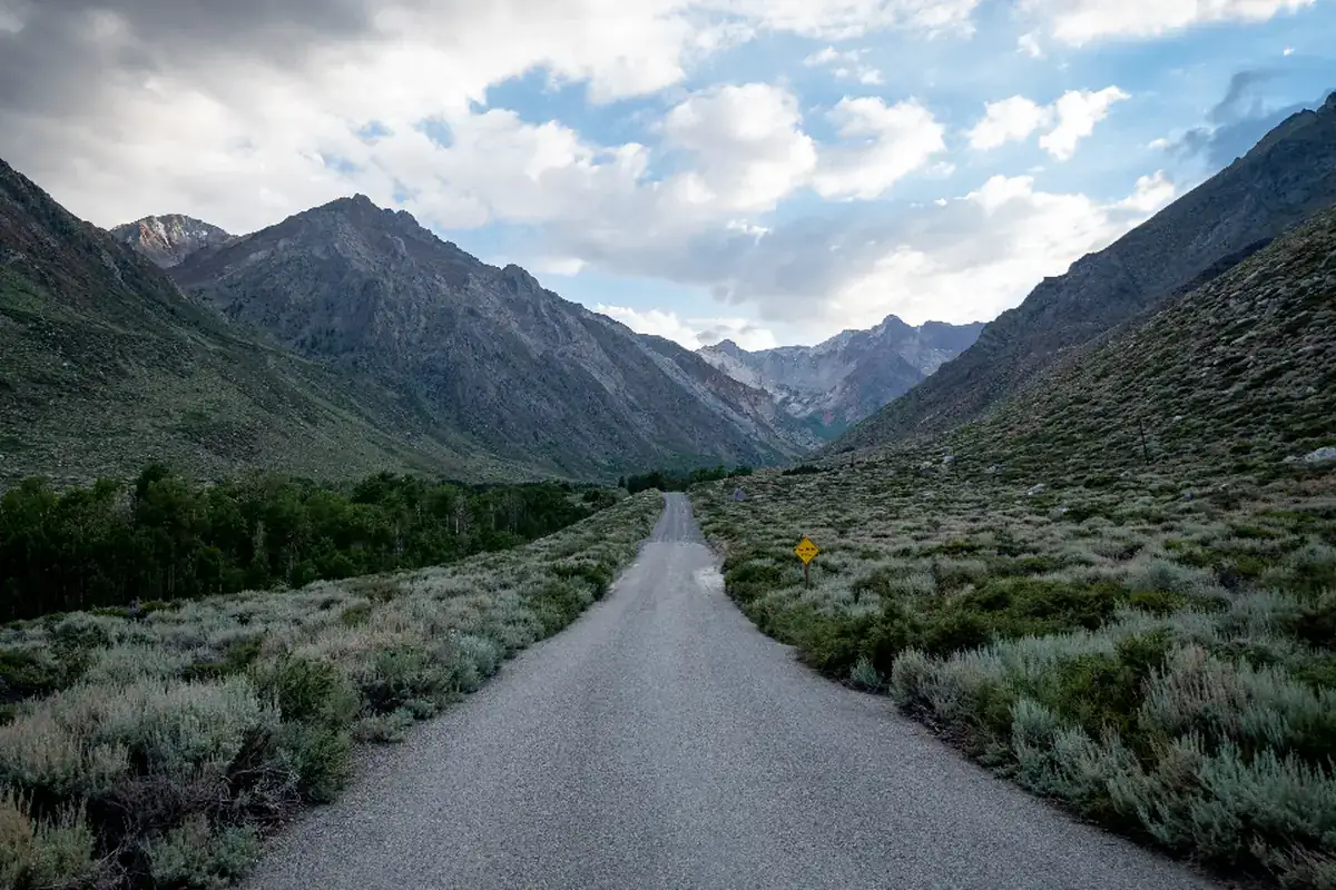 Carretera estrecha y vacía que atraviesa un valle entre montañas bajo un cielo con nubes