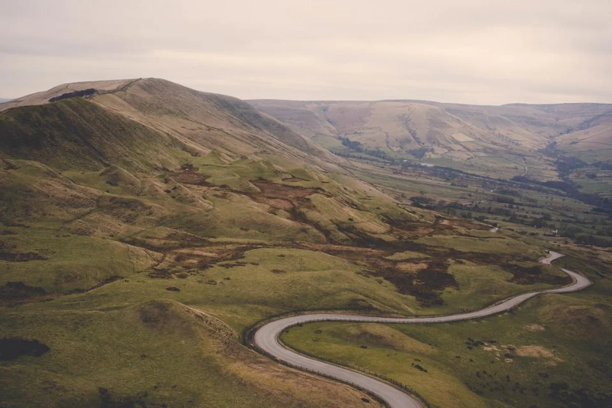 Carretera estrecha que serpentea por un valle entre colinas verdes bajo un cielo nublado