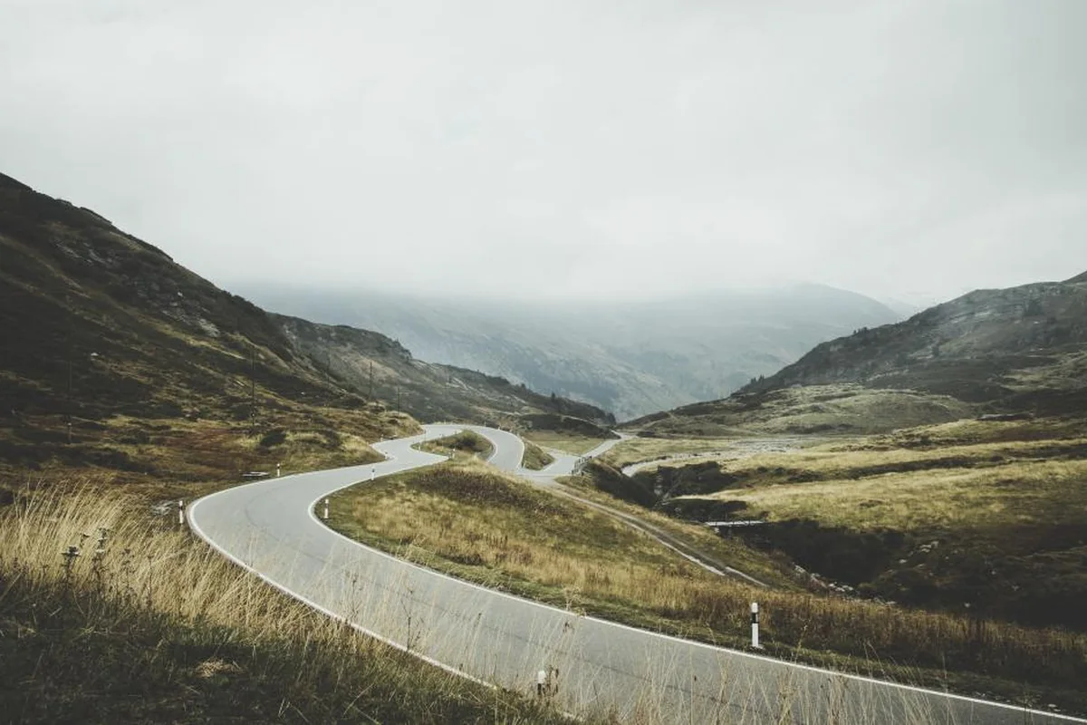 Carretera sinuosa que atraviesa un valle de montaña cubierto de hierba seca, con niebla sobre las cumbres