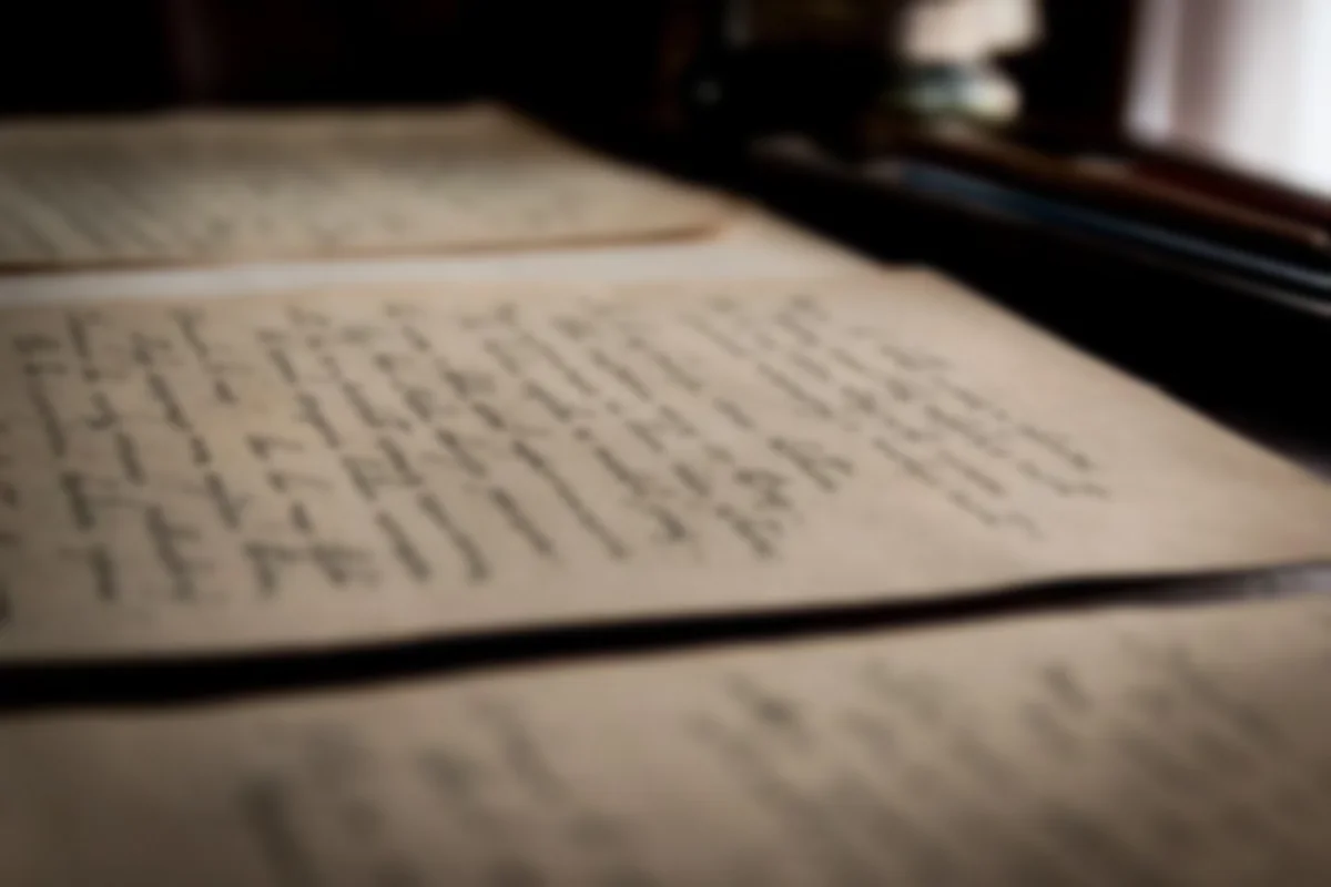 Hojas de papel escritas a mano y desenfocadas sobre una mesa oscura, junto a una ventana con luz suave
