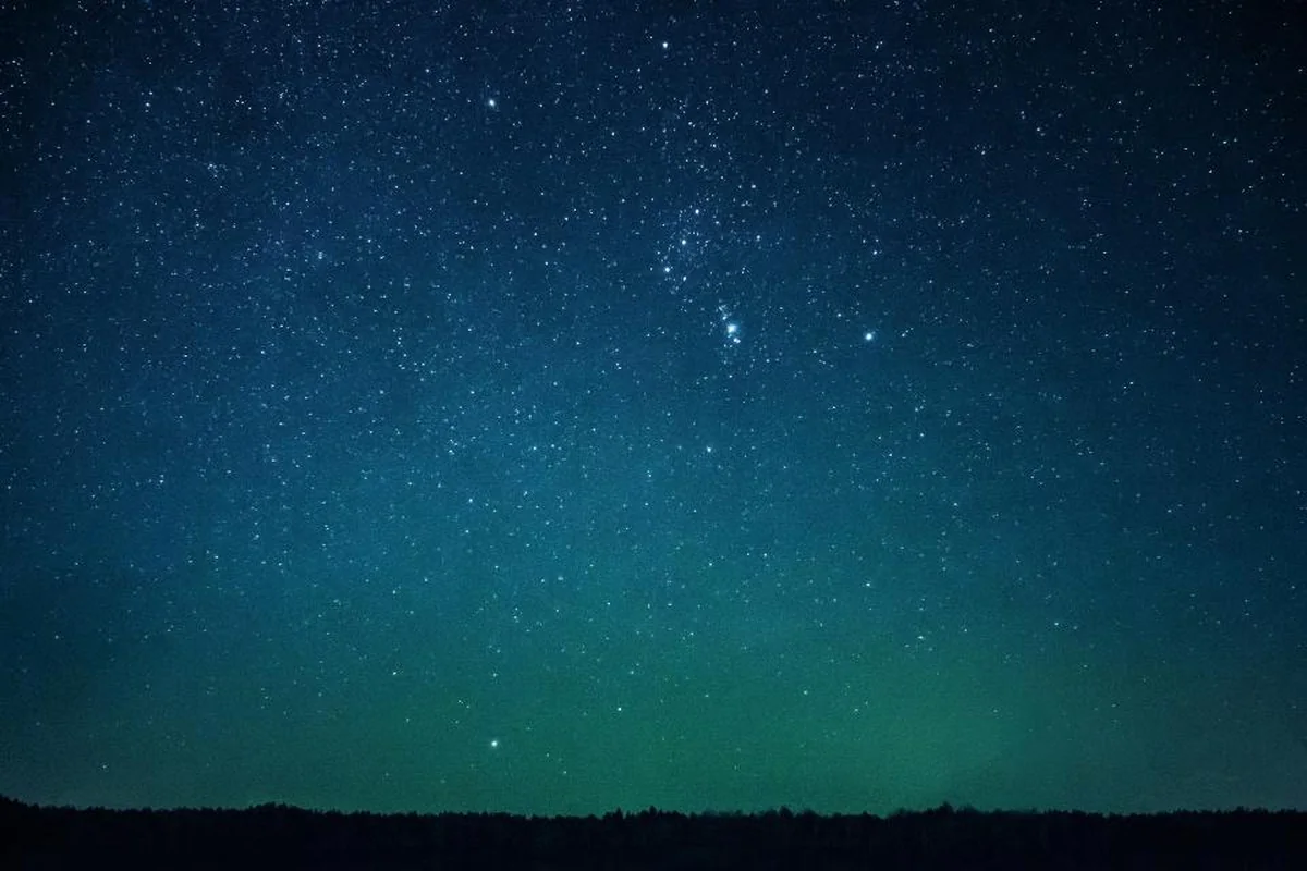 Cielo nocturno estrellado con un leve resplandor en el horizonte