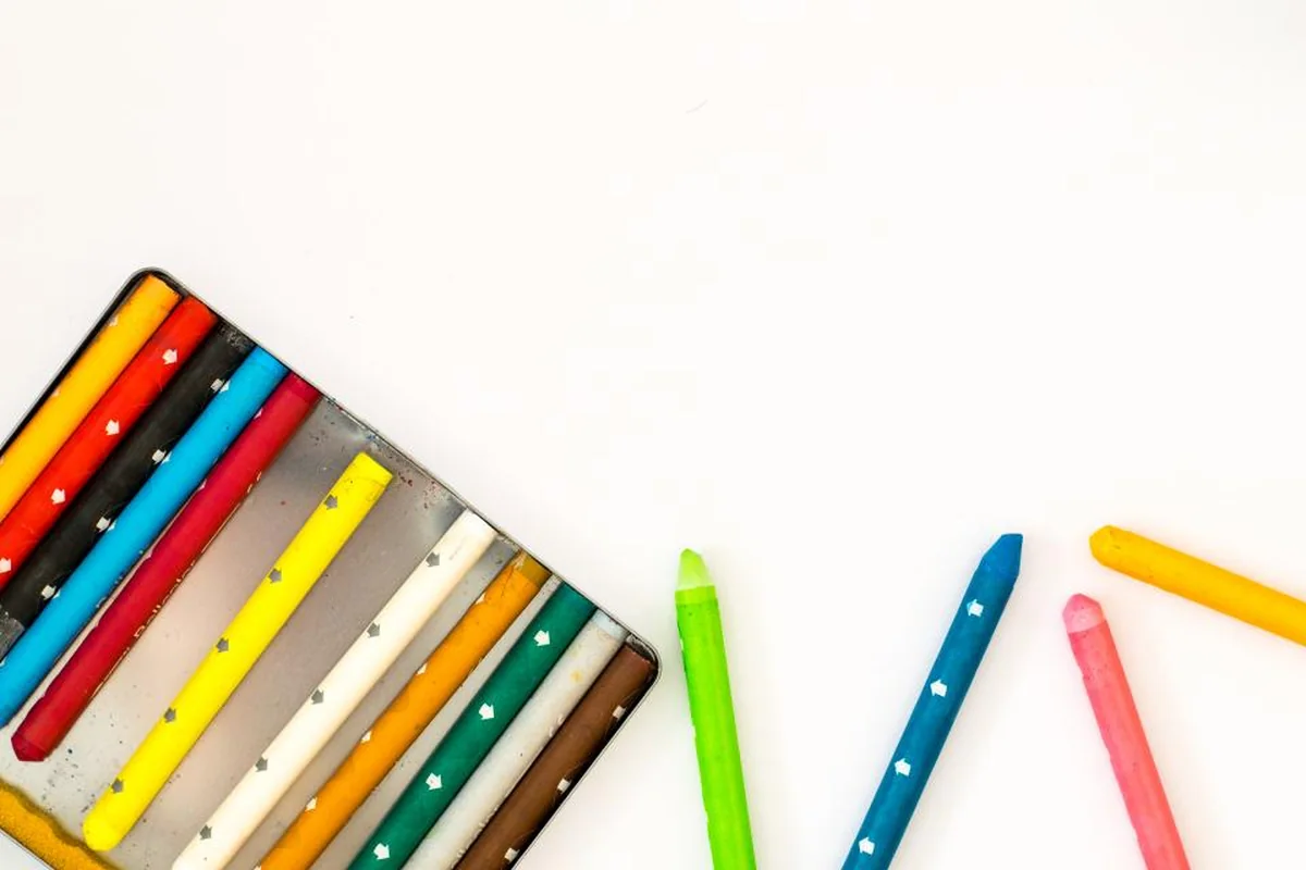 Un estuche metálico con ceras de colores y varias ceras sueltas desordenadas sobre una superficie blanca