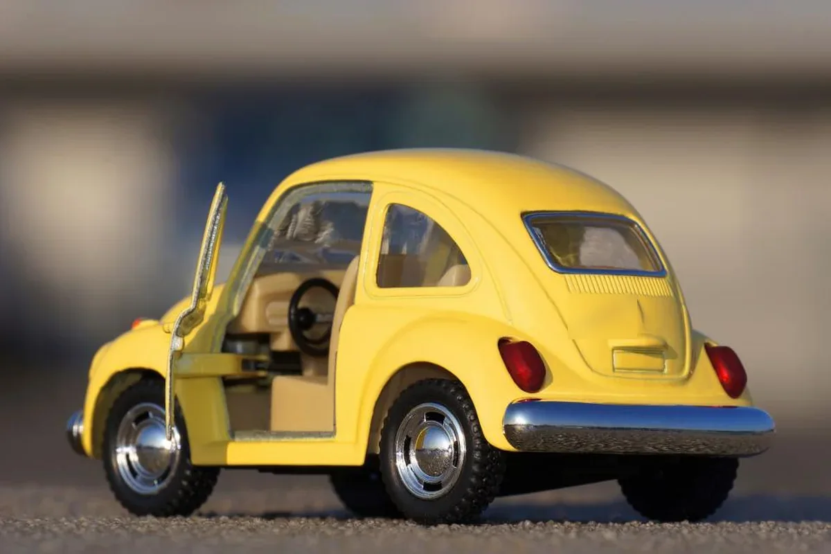 Coche de juguete amarillo de estilo clásico con la puerta del conductor abierta, sobre un fondo desenfocado
