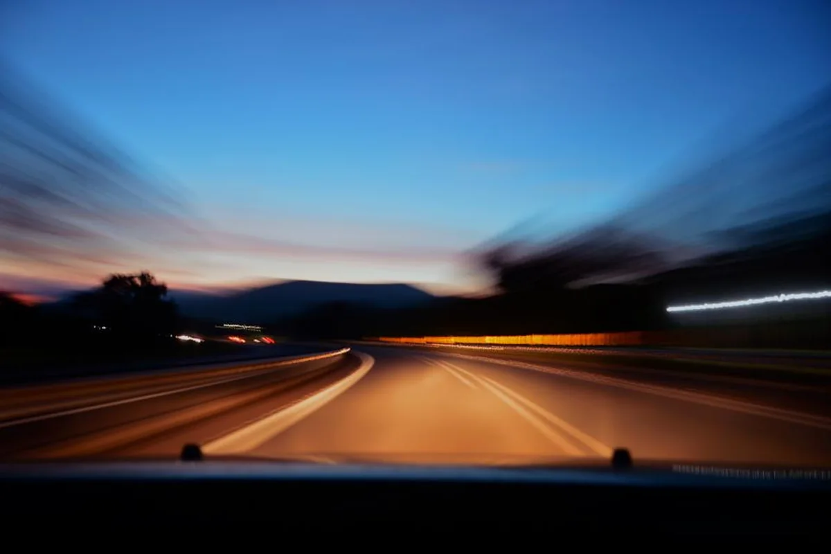 Carretera al atardecer vista desde dentro de un coche en marcha, con el paisaje desenfocado por la velocidad