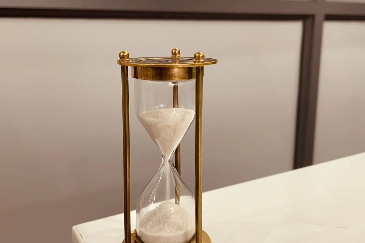 Reloj de arena de latón sobre una mesa blanca, con la arena cayendo