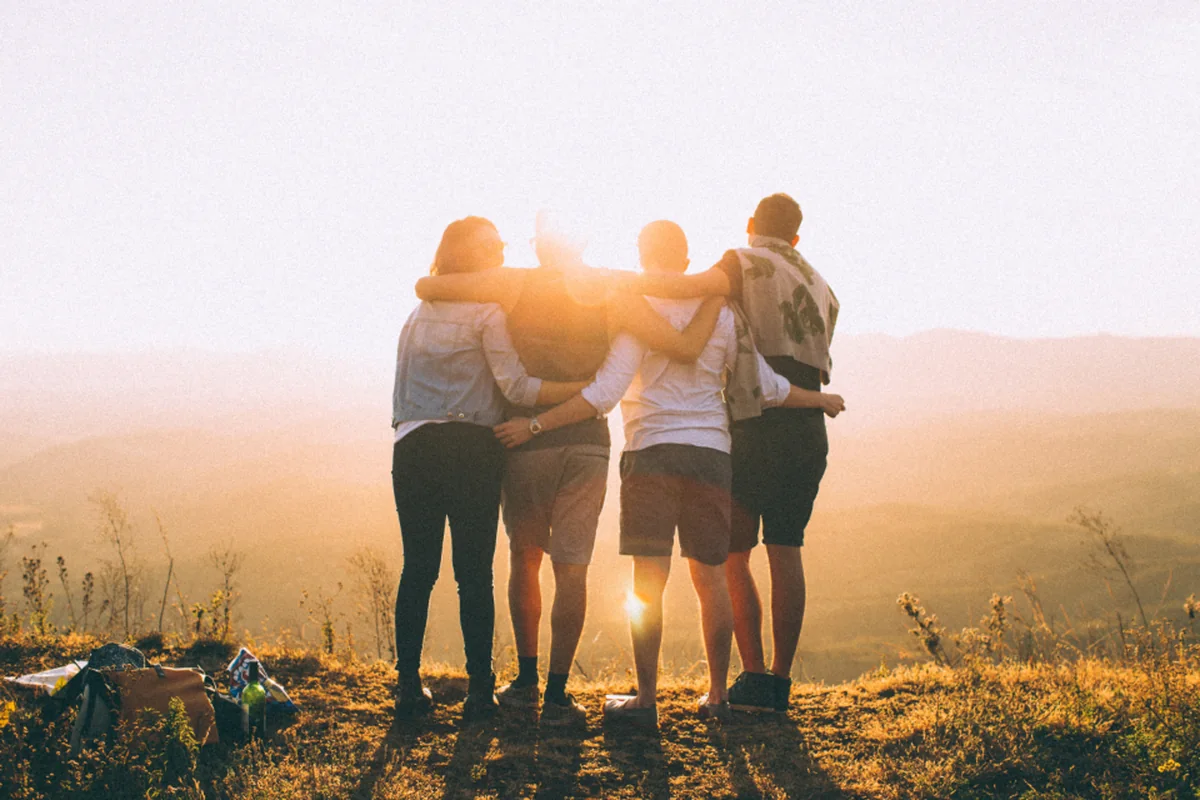 Cuatro personas abrazadas de espaldas contemplando un paisaje al atardecer