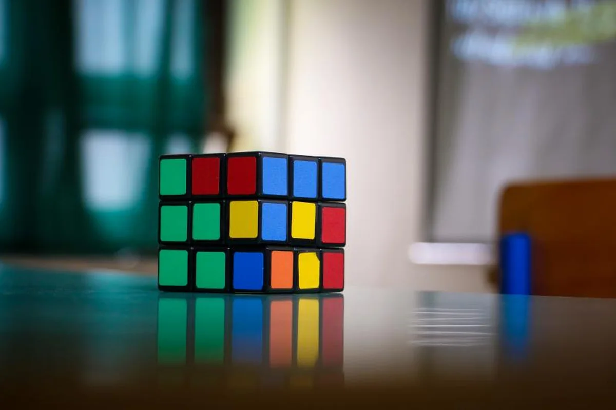 Cubo de Rubik con caras de colores mezcladas sobre una mesa brillante, con el fondo de una habitación desenfocado