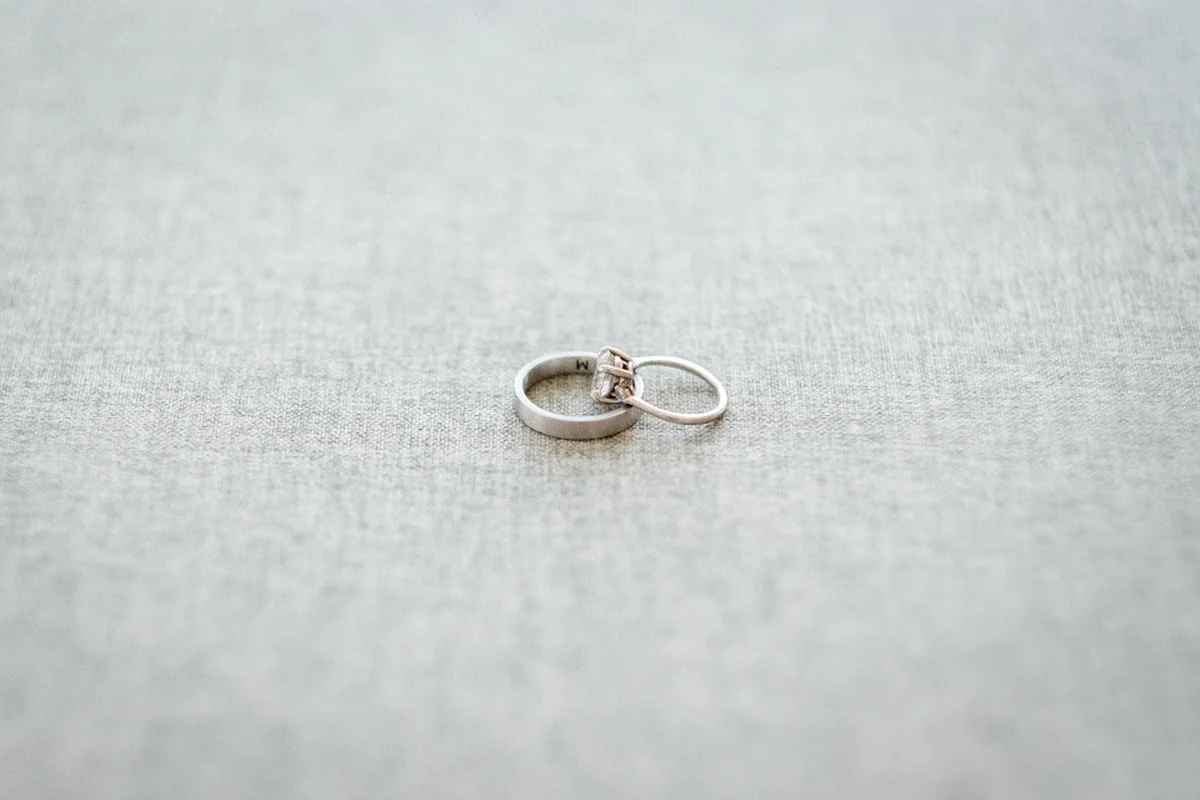 Dos alianzas de boda plateadas apoyadas una sobre otra encima de una tela de lino gris