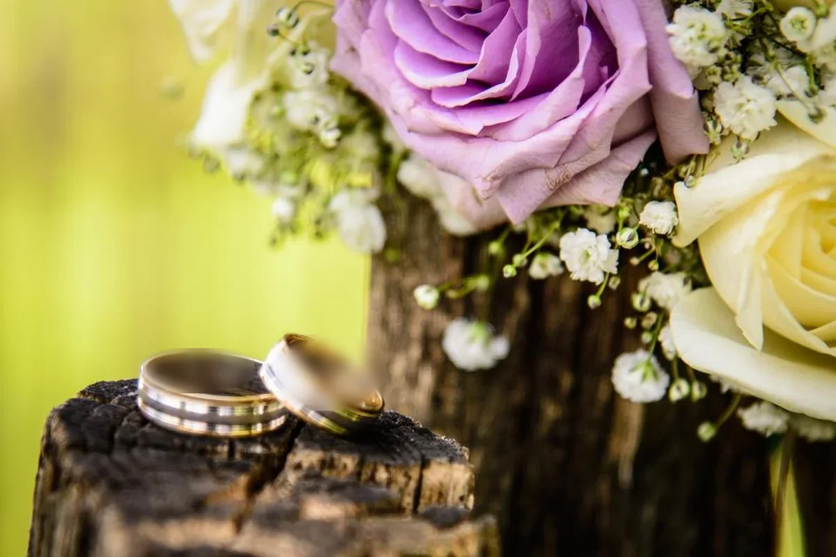 Dos alianzas doradas sobre un tronco de madera junto a un ramo de rosas y flores blancas
