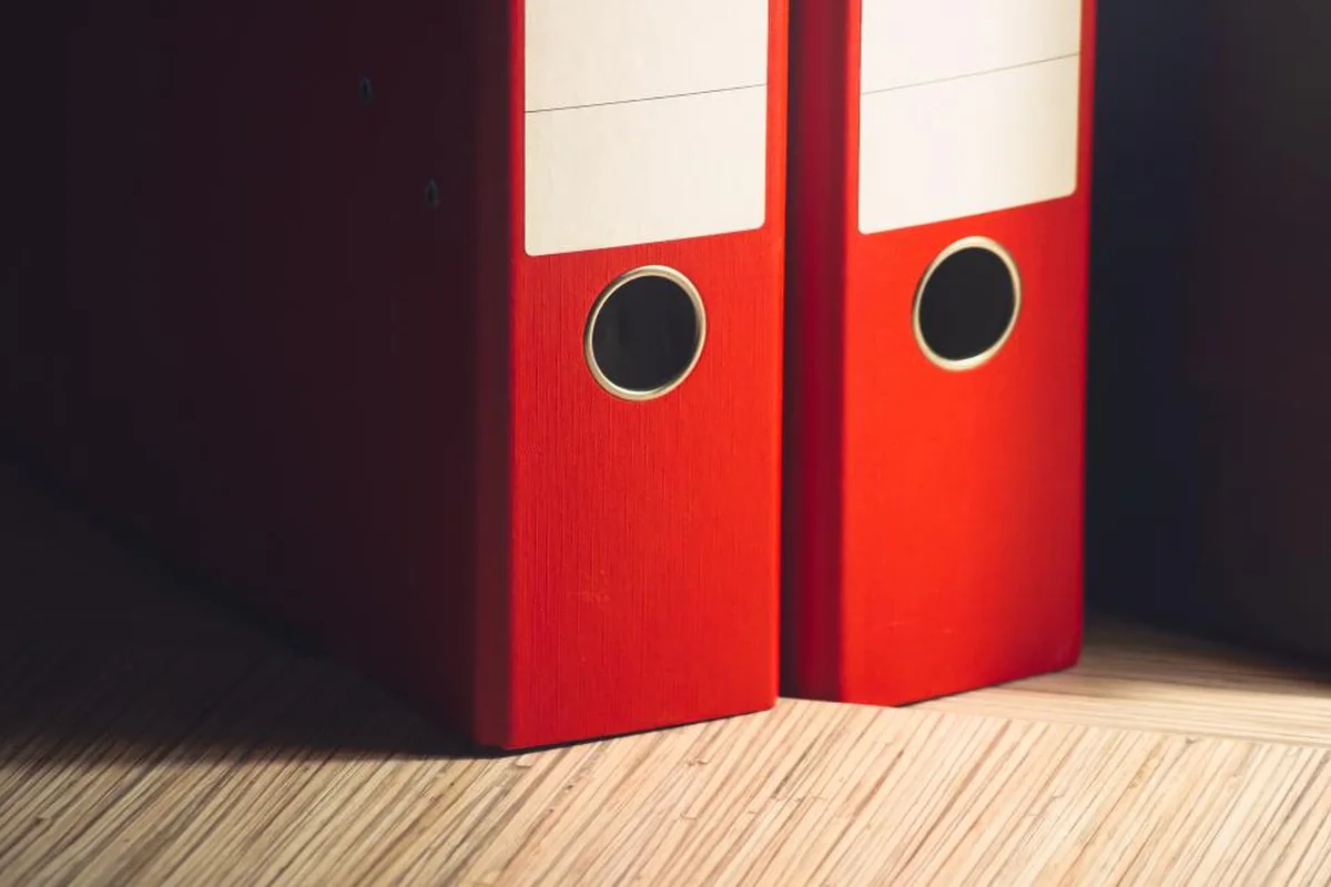 Dos archivadores rojos apoyados sobre un suelo de madera, en penumbra