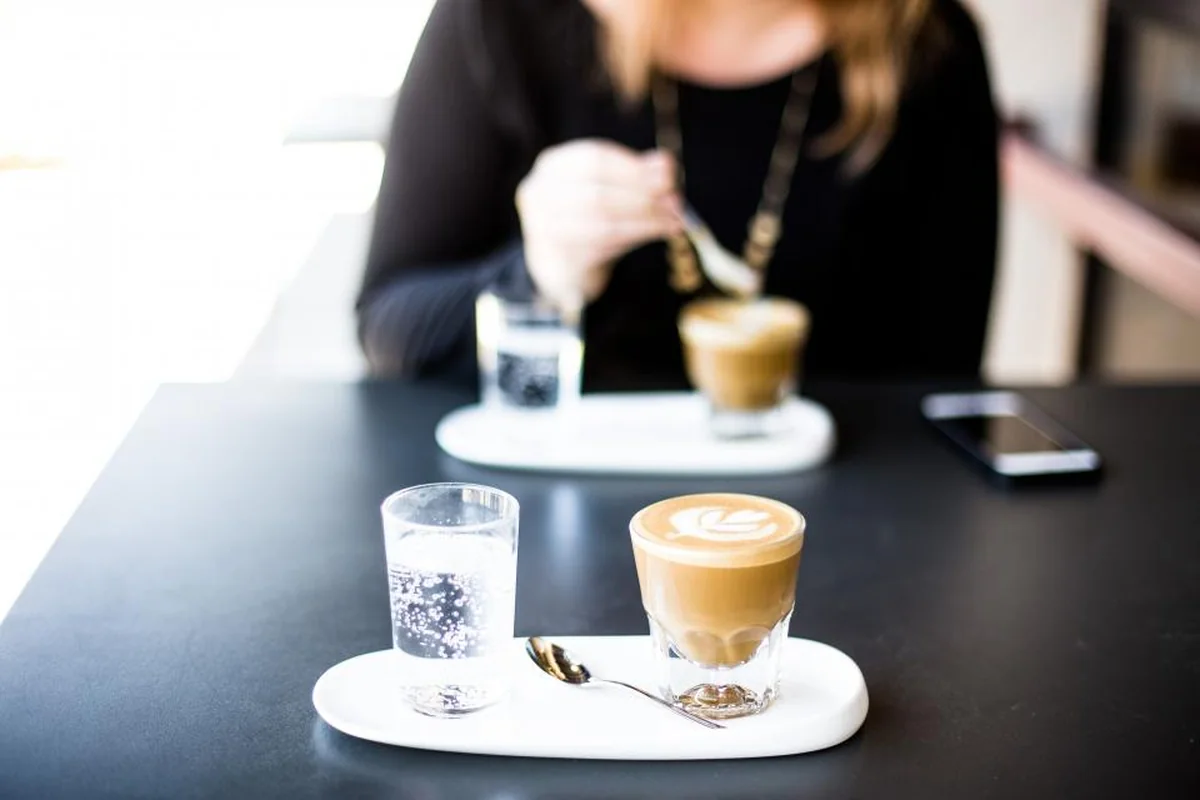 Dos cafés con vasos de agua sobre una mesa negra junto a un teléfono móvil