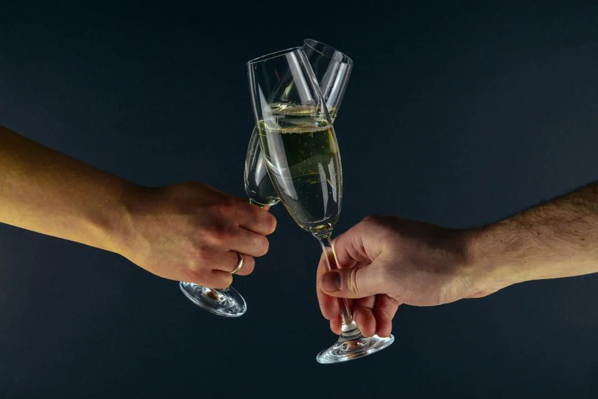 Dos manos que chocan copas de cava sobre un fondo azul oscuro