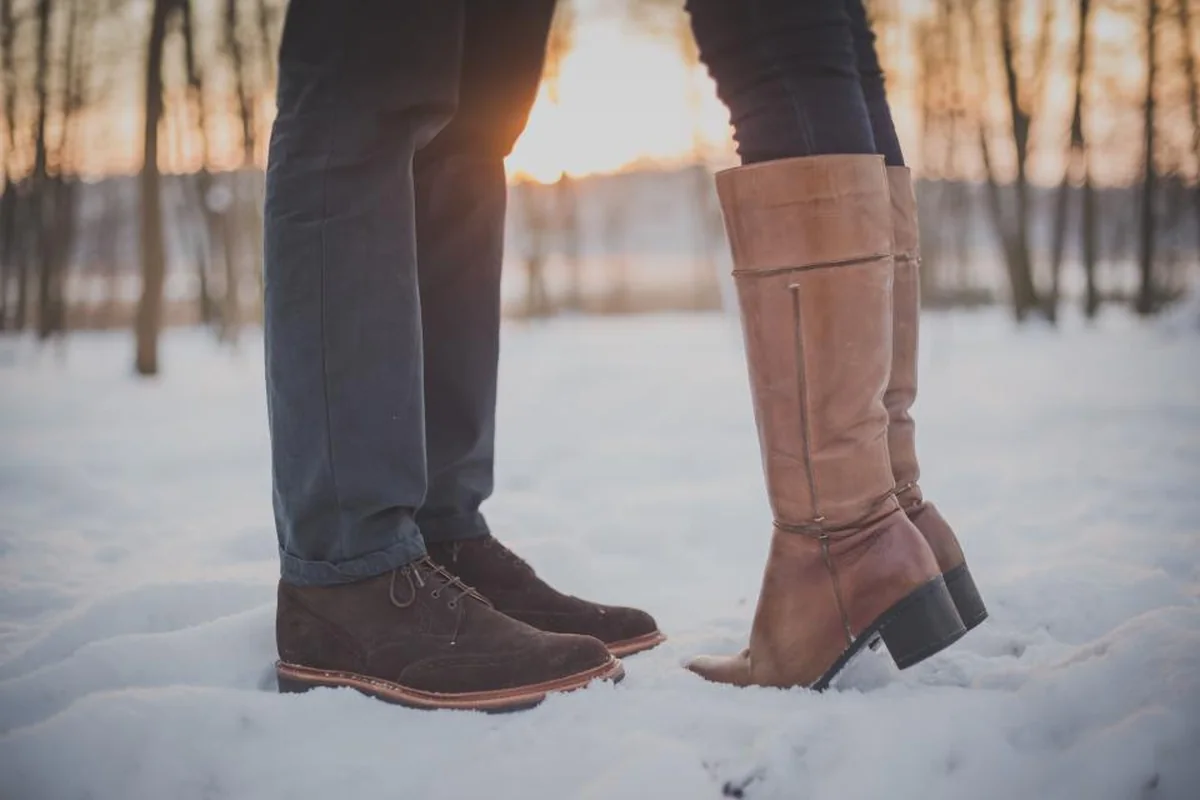 Dos personas de pie frente a frente sobre la nieve, vistas solo de rodillas para abajo, con botas marrones