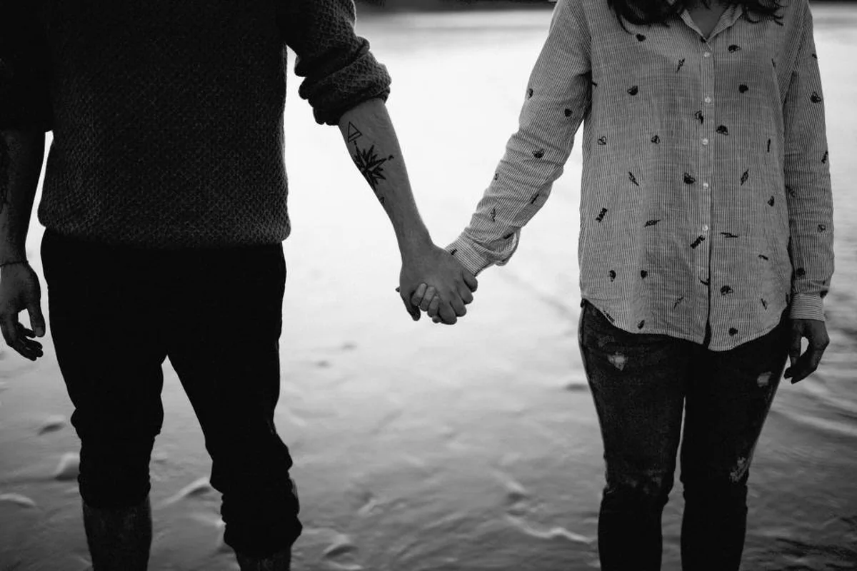 Fotografía en blanco y negro de dos personas caminando cogidas de la mano, vistas de cuello para abajo