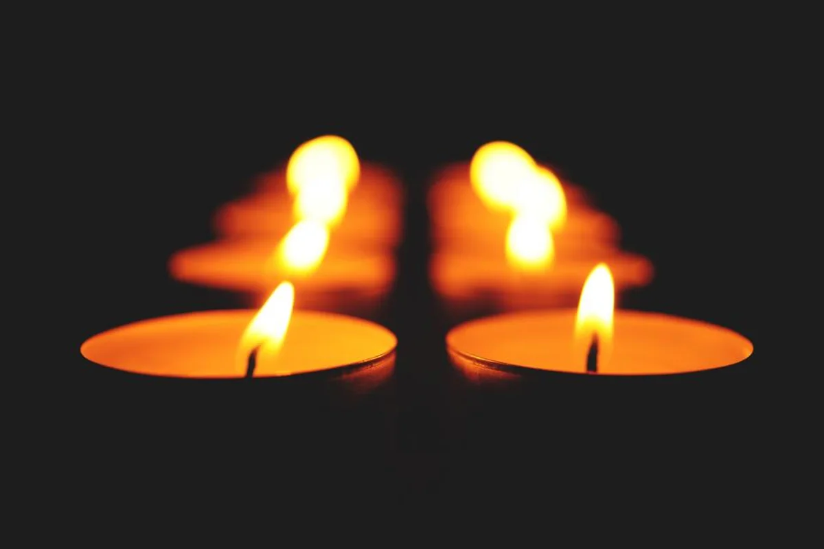 Dos velas pequeñas encendidas sobre un fondo oscuro, con el reflejo desenfocado de sus llamas detrás