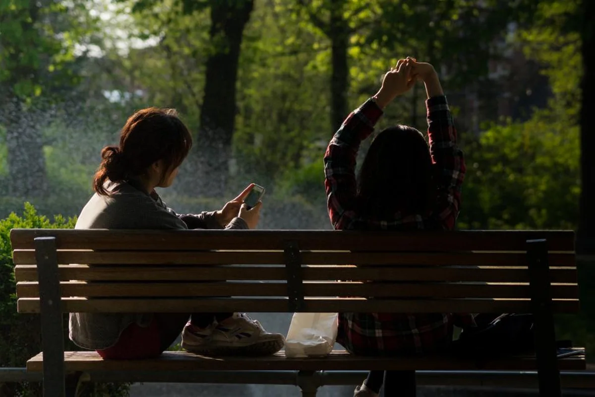 Dos personas sentadas juntas de espaldas en un banco de un parque, en silencio