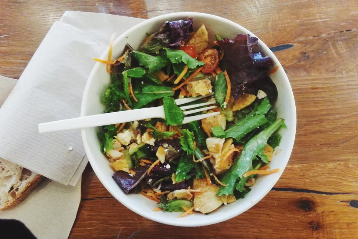 Bol de ensalada con un tenedor sobre una mesa de madera junto a una servilleta de papel