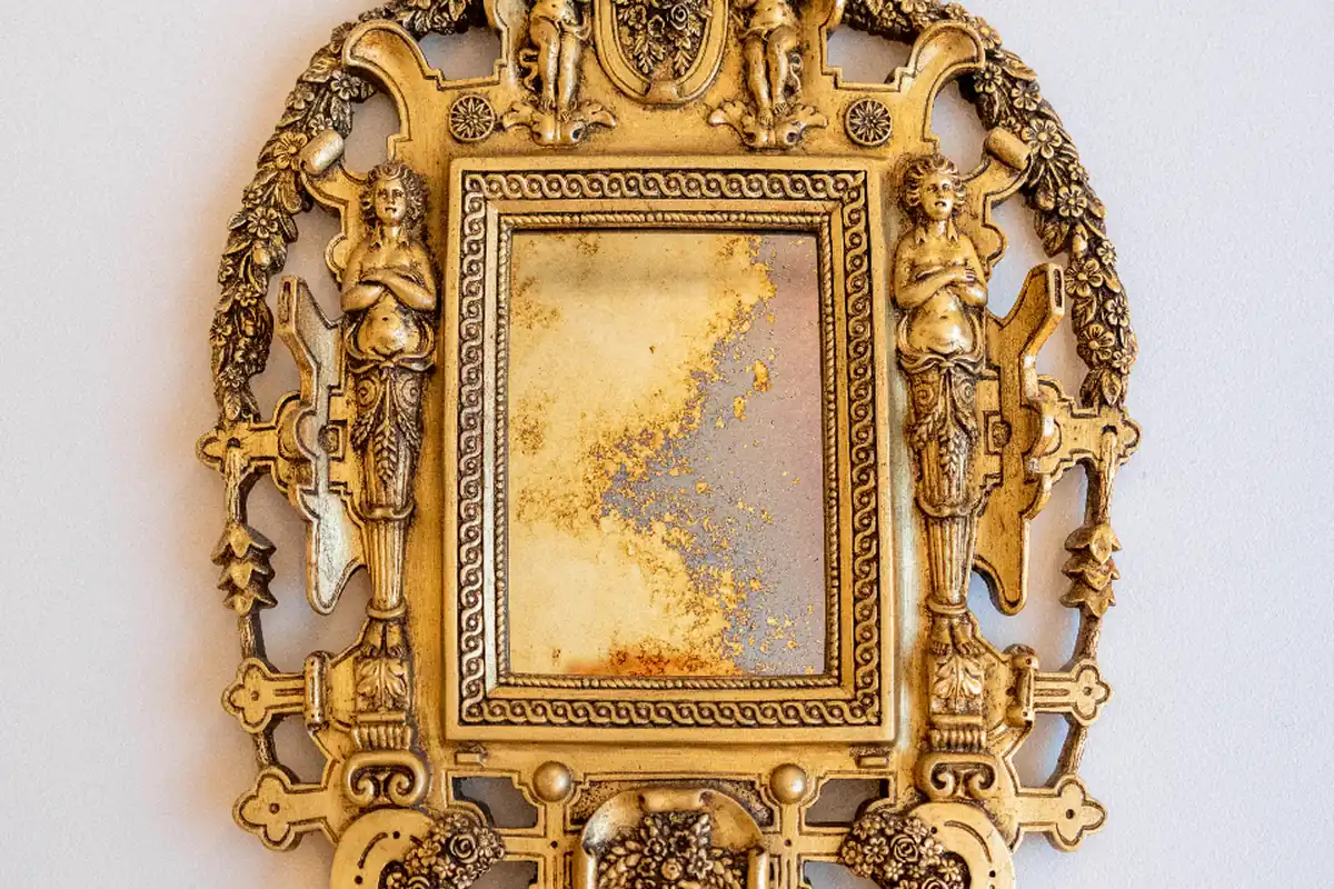 Espejo antiguo con un marco dorado muy ornamentado colgado en una pared blanca