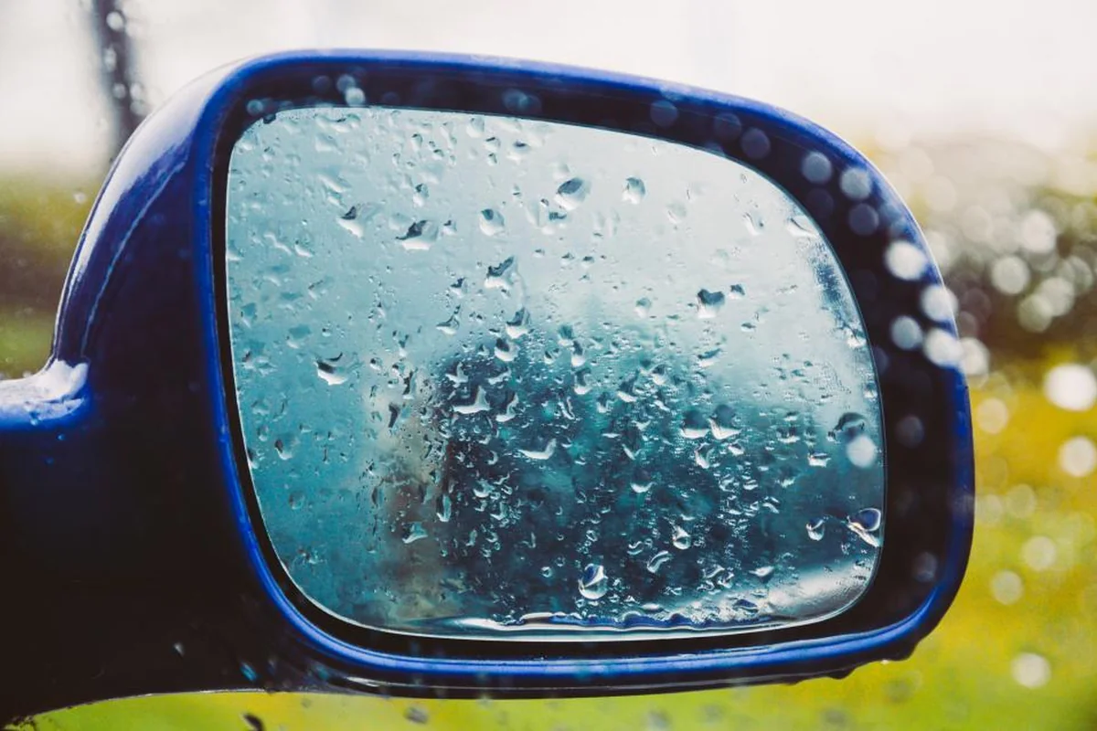Espejo retrovisor azul cubierto de gotas de lluvia que deja ver un reflejo borroso