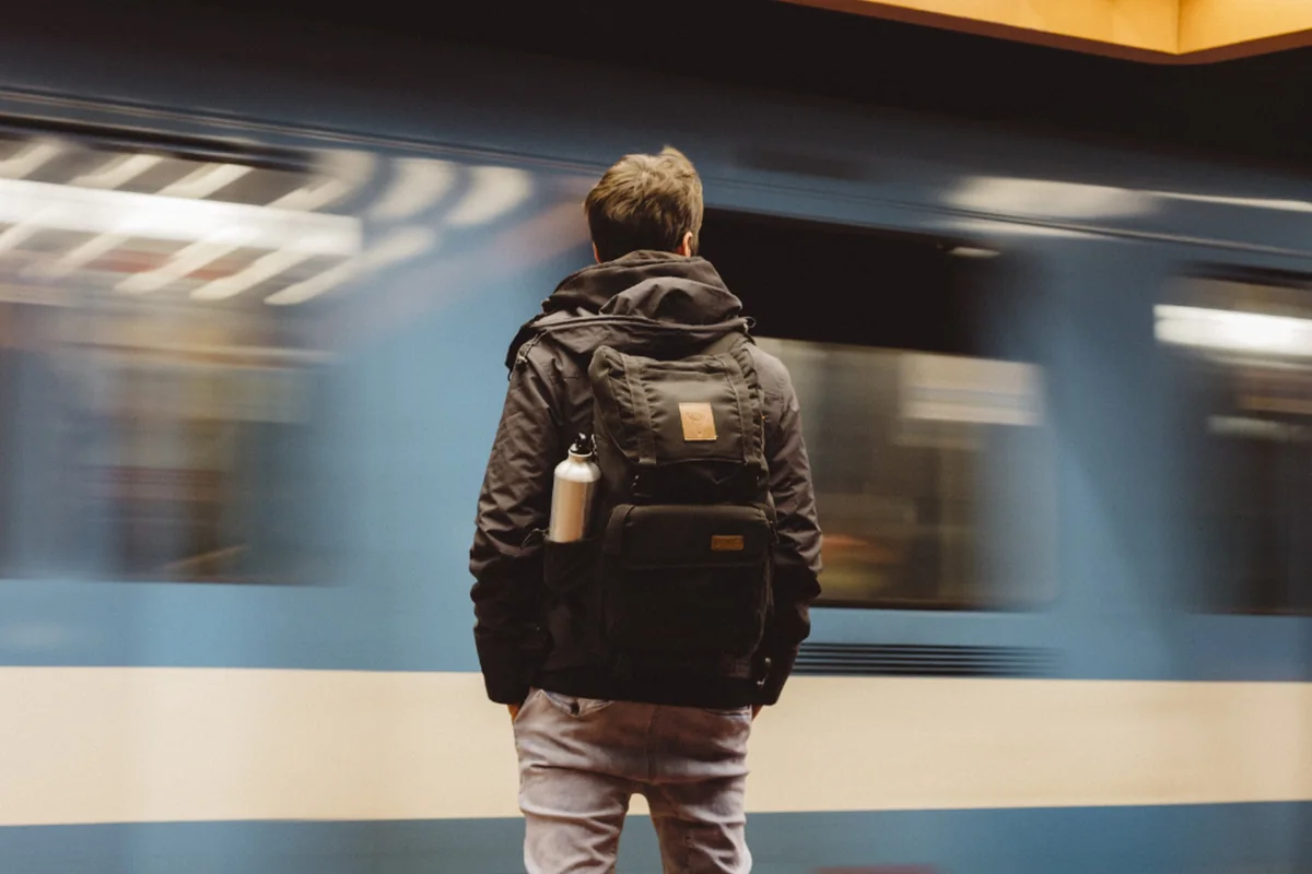 Persona con mochila de espaldas en un andén mientras pasa el tren