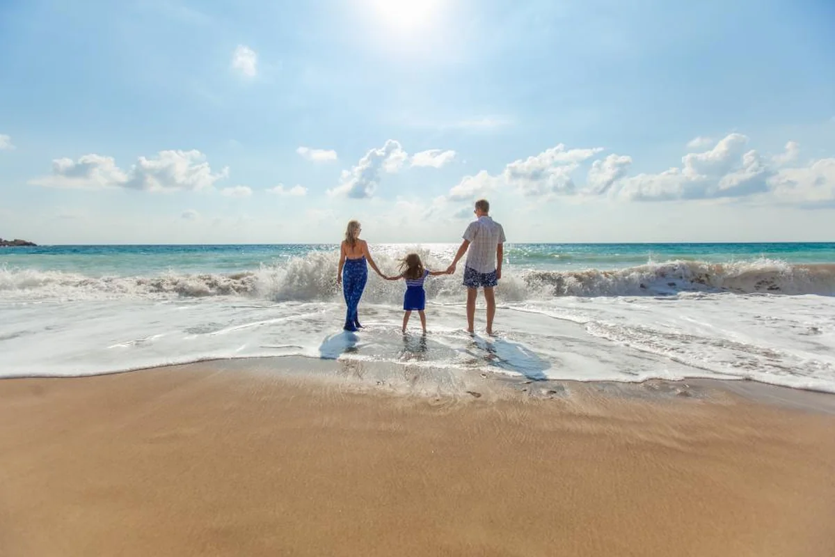 Una mujer, una niña y un hombre de espaldas, cogidos de la mano en la orilla del mar mientras rompen las olas