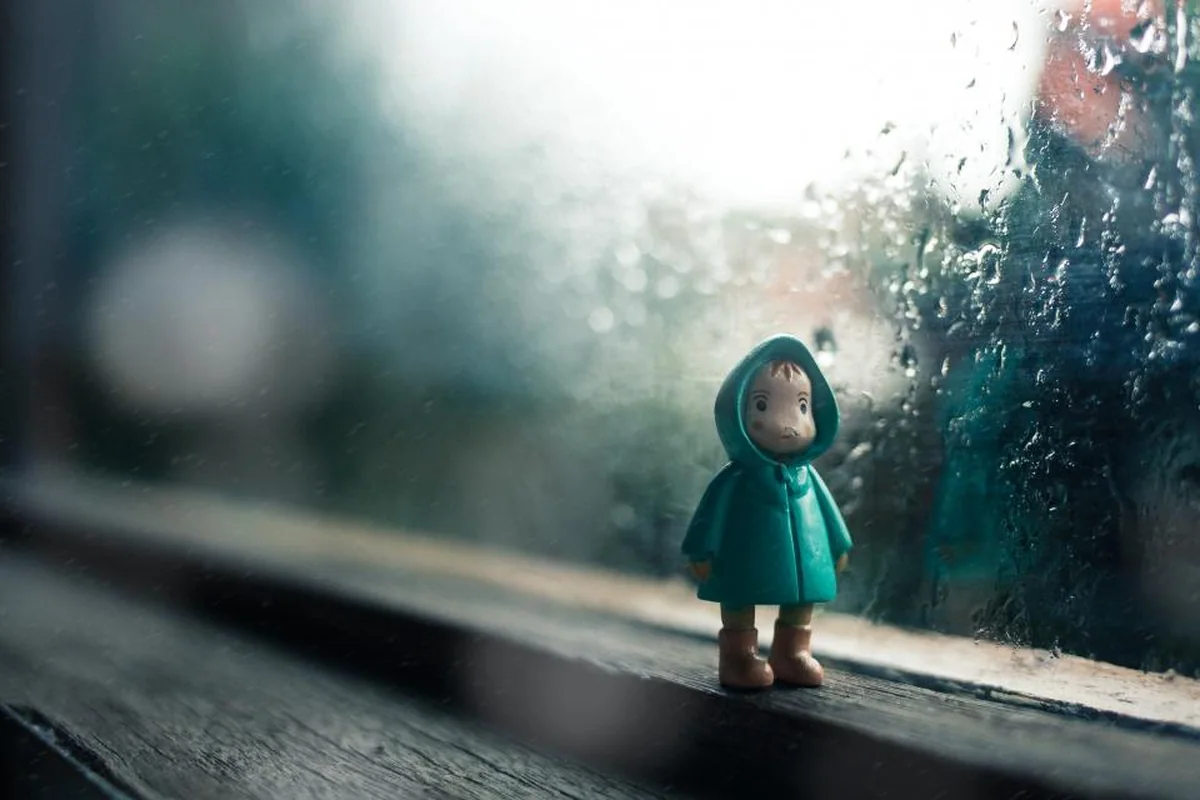 Una pequeña figura de juguete con chubasquero verde junto a una ventana mojada por la lluvia