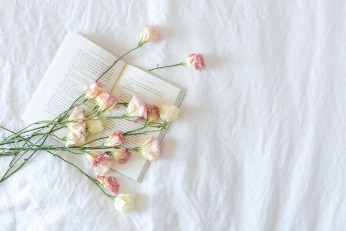 Ramo de flores rosas y blancas sobre un libro abierto encima de unas sábanas blancas arrugadas