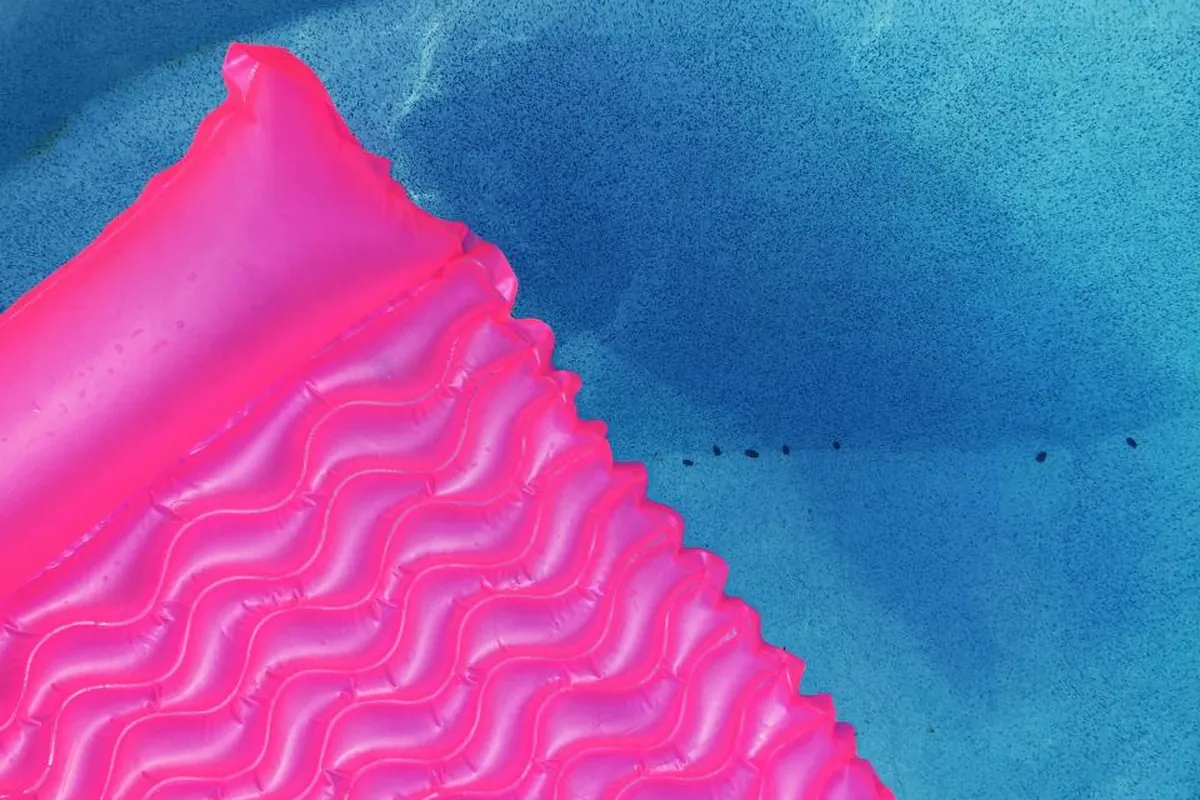 Colchoneta hinchable de color rosa flotando sobre el agua azul de una piscina, vista desde arriba
