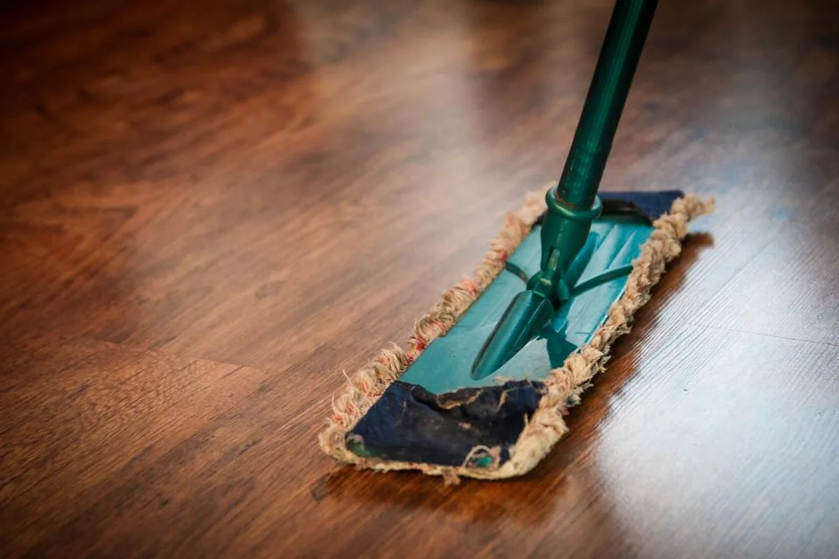 Una mopa de color verde deslizándose sobre un suelo de madera recién fregado que brilla con la luz