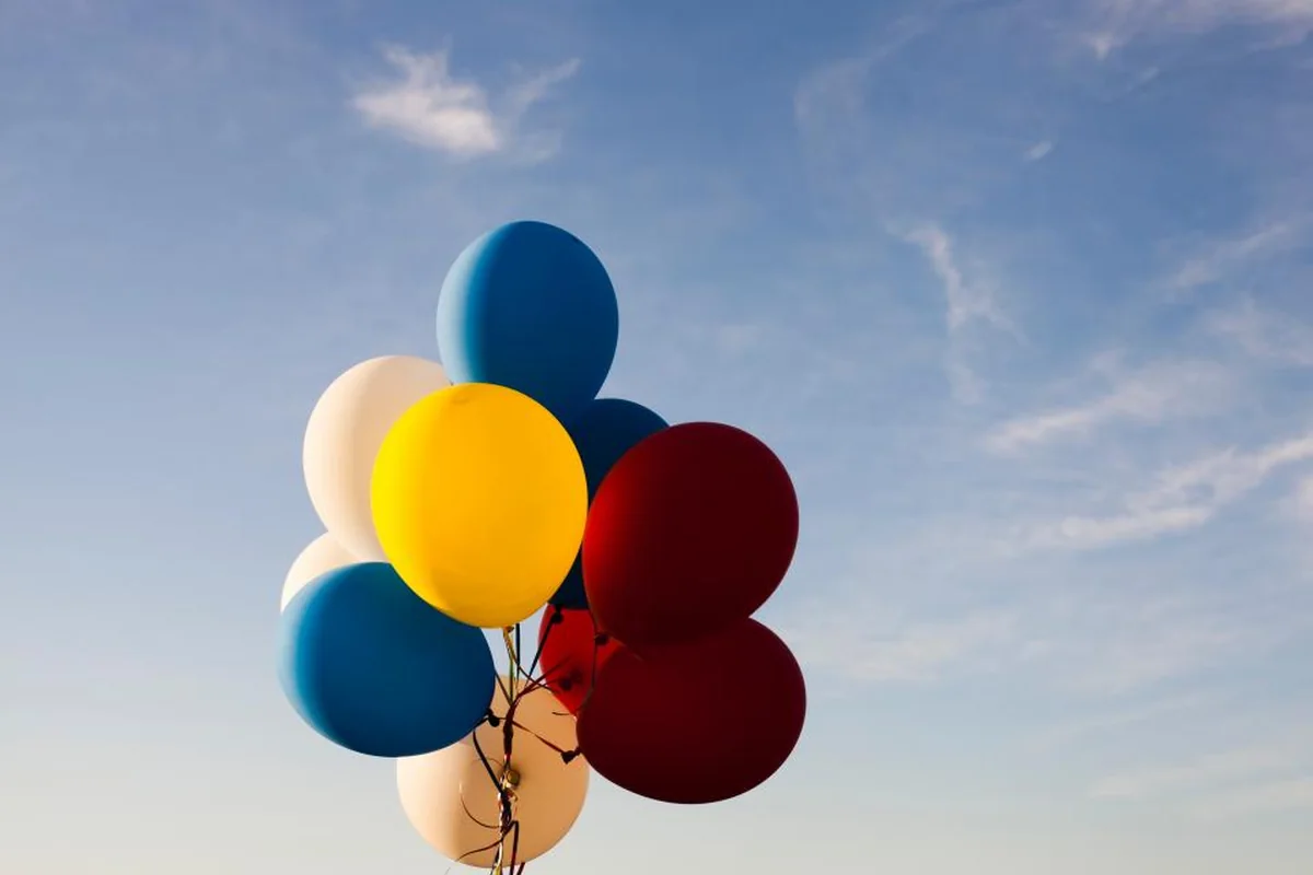 Ramo de globos de colores azul, amarillo, granate y blanco flotando contra un cielo azul con nubes finas