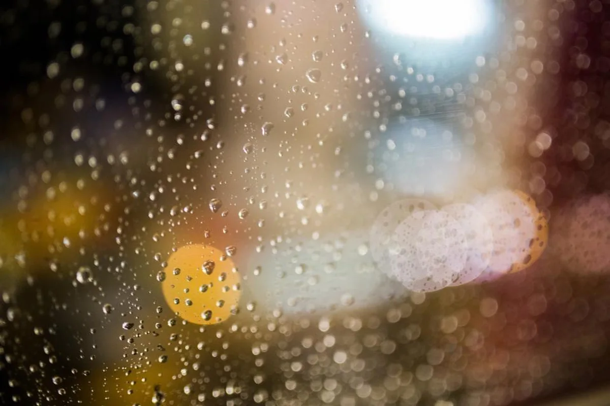 Gotas de lluvia sobre un cristal con luces de la ciudad desenfocadas al fondo, de noche