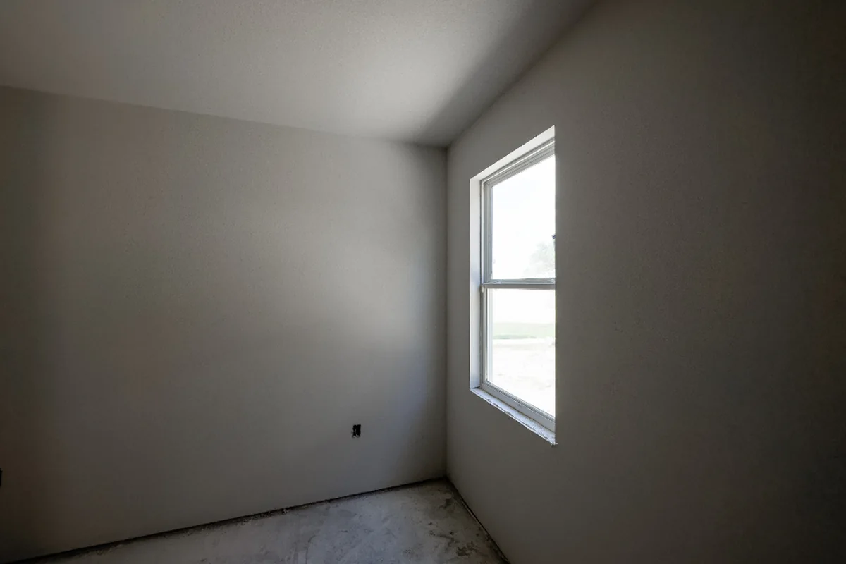 Habitación vacía de paredes blancas con una ventana por la que entra luz natural